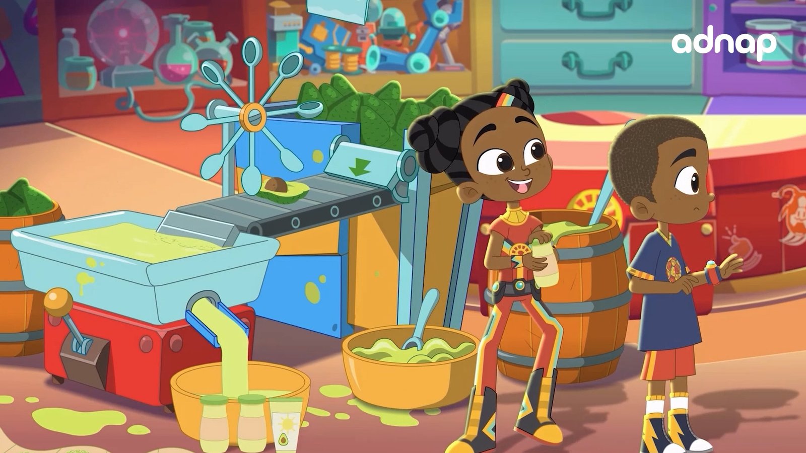 Two children in a colourful cartoon workshop beside a conveyor belt and bowls of green dip